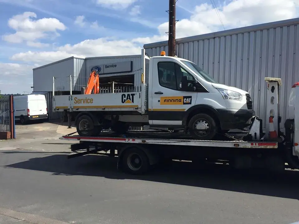 Finning CAT service truck with a mounted crane loaded on a Simpsons flatbed recovery truck at a dealer service yard